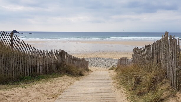 A wooden pathway leading to a beach with a wooden fence on both sides.