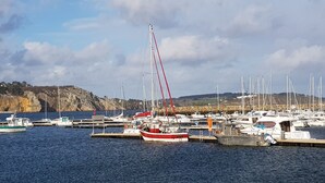 A marina with boats docked, a rocky coastline, and a clear sky.