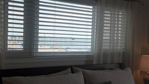 Ein Hotelzimmer mit Bett, einem Fenster mit Jalousien und Blick auf Strand und Steg.