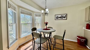 Een eetgedeelte met een ronde tafel, vier stoelen, een kroonluchter en een bord met de tekst 'thankful' aan de muur.