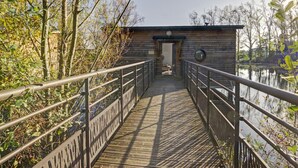 A wooden boardwalk leading to a small wooden structure with a metal railing. - Unique cabin by a pond, pets allowed, private terrace (Veauchette)