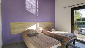 A bedroom with two beds, a wooden headboard, a lamp, and a view of a garden through a glass door. - Unique cabin by a pond, pets allowed, private terrace (Veauchette)