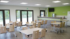 A cafeteria with tables and chairs, a kitchen area, and a large window. - Unique cabin by a pond, pets allowed, private terrace (Veauchette)