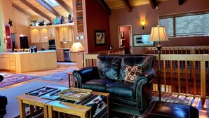 A cozy living room with a leather sofa, wooden coffee table, and a dining area with wooden cabinets and a kitchen island. - Meadows Hideaway with Access to Exclusive Golf (Sunriver)