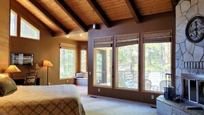 A bedroom with a large bed, multiple windows, a fireplace, and a stone wall. - Meadows Hideaway with Access to Exclusive Golf (Sunriver)
