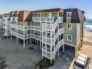 A row of multi-story beach cottages with balconies, a parking area, and a view of the ocean. - Take It E-Sea | Oceanfront + Community Pool! (Kure Beach)