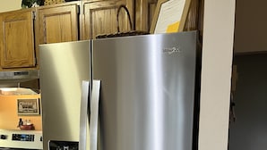 Ruostumattomasta teräksestä valmistettu Whirlpool-jääkaappi keittiössä, jossa on puukaapit ja sisäänrakennettu uuni.
