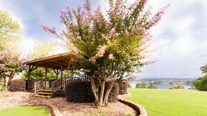A gazebo with a wooden staircase, surrounded by a brick border and a tree with pink flowers.