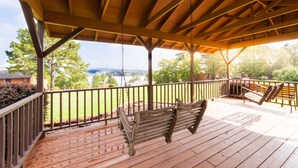 A wooden deck with a swing and two lounge chairs, overlooking a grassy area and a body of water.