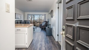 A modern kitchen with white cabinets and a wooden countertop, leading to a dining area with a dark leather chair and a table.