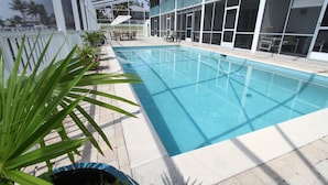 En swimmingpool med ett kaklat poolområde, omgiven av planterade växter i krukor och en överbyggd sittplats.