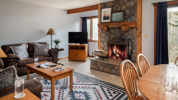 Una sala de estar acogedora con chimenea de piedra, un televisor, una mesa de comedor con sillas y una alfombra estampada.