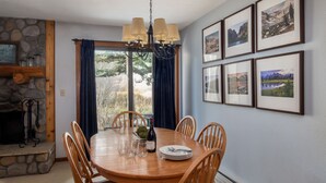 Un comedor con una mesa redonda de madera, seis sillas, una lámpara de araña, una chimenea y cuadros enmarcados en la pared.