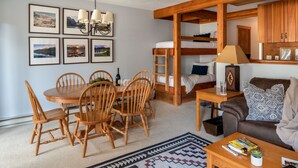 Una habitación acogedora con una mesa de madera para comer, sillas, una cama litera, un sofá y una mesita de centro.