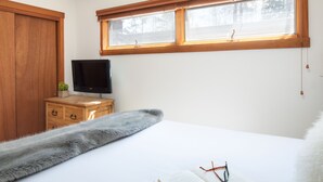 Un dormitorio con una cama, un televisor sobre una cómoda de madera, una ventana con persianas y una manta suave.