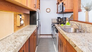 Una cocina compacta con armarios de madera, un lavamanos de acero inoxidable y un microondas.