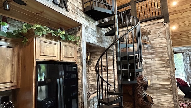 Un intérieur rustique avec un escalier en bois, un réfrigérateur noir et une statue d’ours.