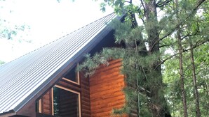 Une cabane en rondins avec un toit en pente, un revêtement extérieur en bois et une véranda équipée de deux chaises et d’une table.