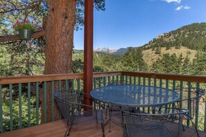Une terrasse en bois avec une table et des chaises rondes en métal, offrant une vue sur un paysage montagneux.