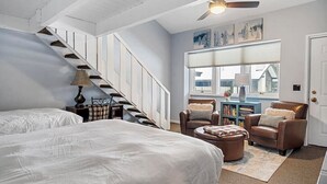 Un dormitorio con una cama grande, un aparador, un escritorio y una silla. Hay una ventana con persianas y vistas al exterior.