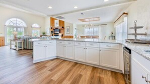 A spacious kitchen with a large island, wooden flooring, and a view to the dining area. - The Colman at Ships Watch in Duck (Duck)