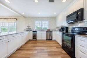 A kitchen with white cabinets, a stainless steel range hood, and a black microwave. - The Colman at Ships Watch in Duck (Duck)