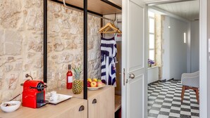 Une pièce avec un mur en pierre, un bureau en bois sur lequel se trouve une machine à café rouge, une assiette de fruits et un vêtement suspendu.