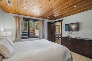 A bedroom with a wooden ceiling, a bed, a dresser, a TV, and a window with curtains.