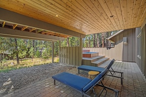 A covered outdoor seating area with lounge chairs, a wooden ceiling, and a view of a forested area. - Nature Retreat with Access to Exclusive Golf (Sunriver)