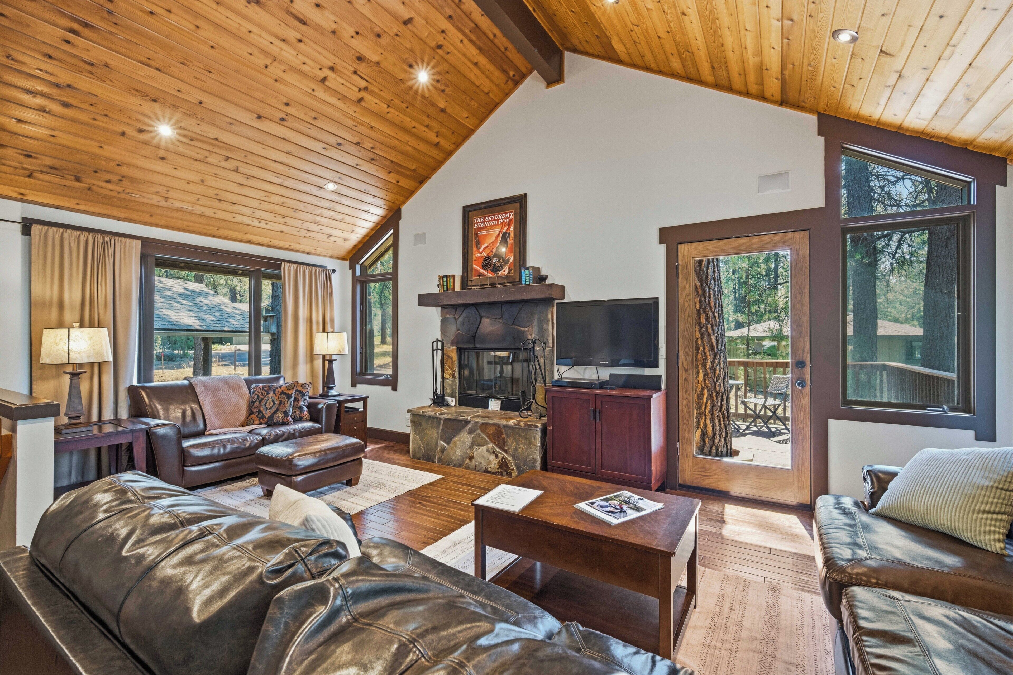 A spacious living room with a stone fireplace, leather furniture, and large windows offering a view of the outdoors.