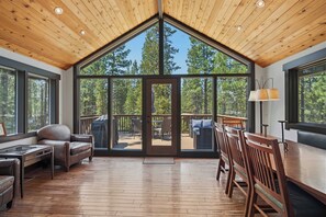 A spacious room with a high ceiling, large windows, a wooden deck, and a dining area. - Nature Retreat with Access to Exclusive Golf (Sunriver)