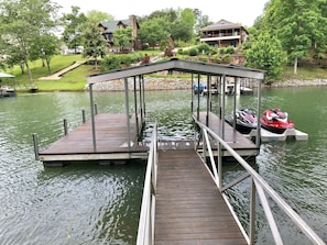 Enjoy serene lakeside views from the covered seating area, accessible via a wooden dock with a metal railing.
