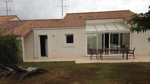 A house with a tiled roof, a sliding glass door leading to a patio, and a small door. There are two lounge chairs on the grass. - INDIVIDUAL HOUSE 110 m2 (ground floor + upper floor) CLOSED GARDEN. GARAGE + outdoor parking (Olonne-sur-Mer)