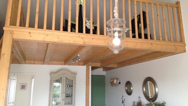 A loft bedroom with a wooden balcony, a hanging light fixture, and a traditional cabinet in the adjacent room. - INDIVIDUAL HOUSE 110 m2 (ground floor + upper floor) CLOSED GARDEN. GARAGE + outdoor parking (Olonne-sur-Mer)