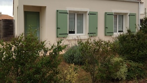 A two-story building with a tiled roof, green shutters, and a small garden in front. - INDIVIDUAL HOUSE 110 m2 (ground floor + upper floor) CLOSED GARDEN. GARAGE + outdoor parking (Olonne-sur-Mer)