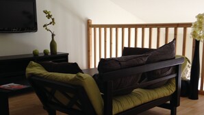 A small, cozy room with a wooden bed, a television on the wall, and a small table with a vase of flowers. - INDIVIDUAL HOUSE 110 m2 (ground floor + upper floor) CLOSED GARDEN. GARAGE + outdoor parking (Olonne-sur-Mer)