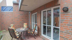 Eine Terrasse mit einer Ziegelwand, einer Glastür und einem Tisch mit Stühlen.