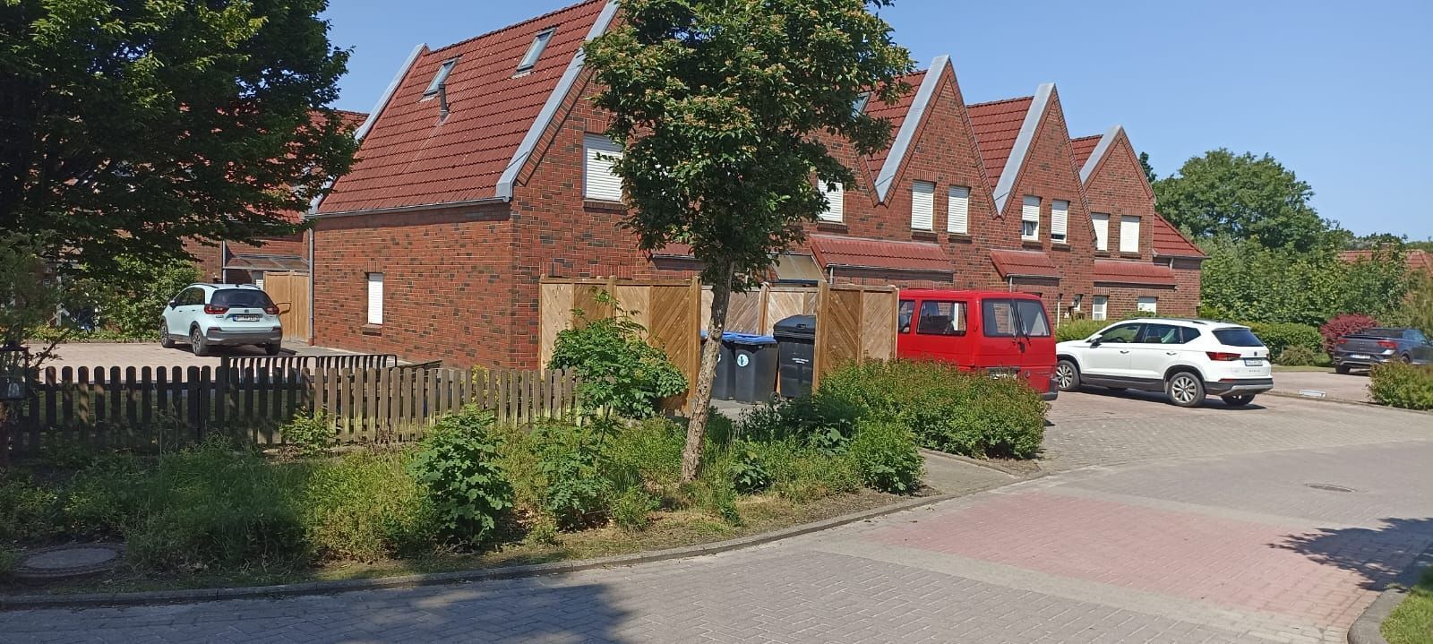 Ein Wohngebiet mit Backsteinhäusern, einem roten Lieferwagen und geparkten Autos.