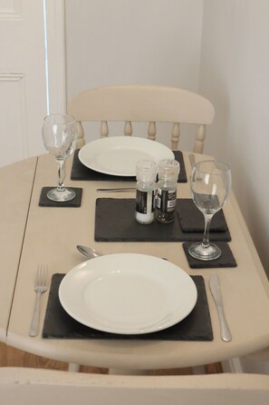A dining table for two, set with a plate, wine glass, fork, and knife on black placemats.