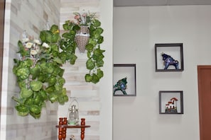 Un couloir avec un mur en bois, une plante suspendue, une petite table sur laquelle est posée une lanterne, et des tableaux encadrés accrochés au mur.