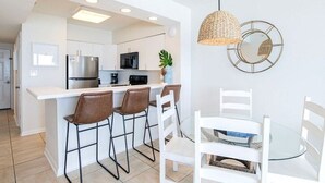 A modern kitchen with white cabinets, a stainless steel refrigerator, and a bar area with stools. - Silver Beach 404 | OBA Beach front condo! Pet Friendly! (Orange Beach)