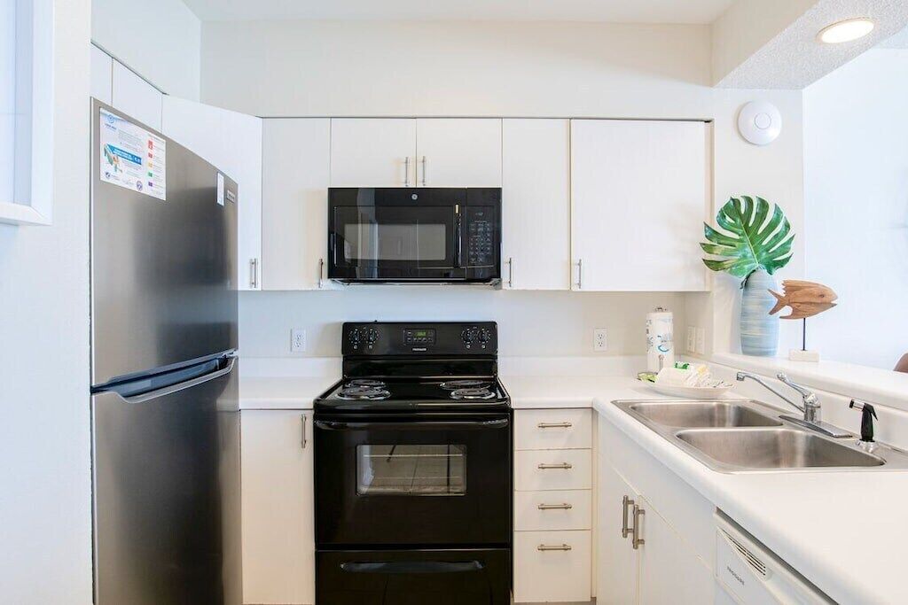 A modern kitchen with white cabinets, a stainless steel refrigerator, a black microwave, and a stove.