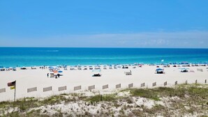 A beach with white sand, clear blue water, and a few umbrellas. - Silver Beach 404 | OBA Beach front condo! Pet Friendly! (Orange Beach)
