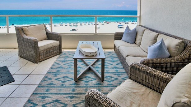 A balcony with wicker furniture, a table, and a view of the beach. - Silver Beach 404 | OBA Beach front condo! Pet Friendly! (Orange Beach)