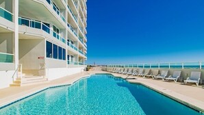 A swimming pool with lounge chairs and a building with multiple balconies. - Silver Beach 404 | OBA Beach front condo! Pet Friendly! (Orange Beach)
