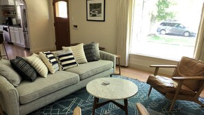 Ein Wohnzimmer mit grauem Sofa, gemusterten Kissen, einem runden Couchtisch und einem Ledersessel.