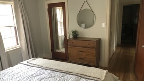 Ein Schlafzimmer mit einem Bett, einem Schminktisch, einem Spiegel und einer Tür zu einem anderen Raum.