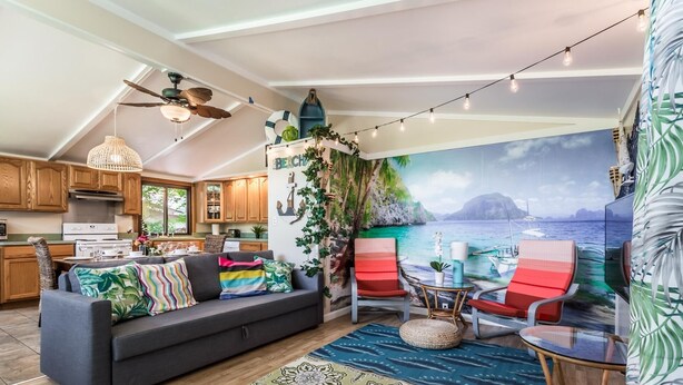Un espacio de sala acogedor con sofá, sillas y vista al mar a través de un ventanal grande.