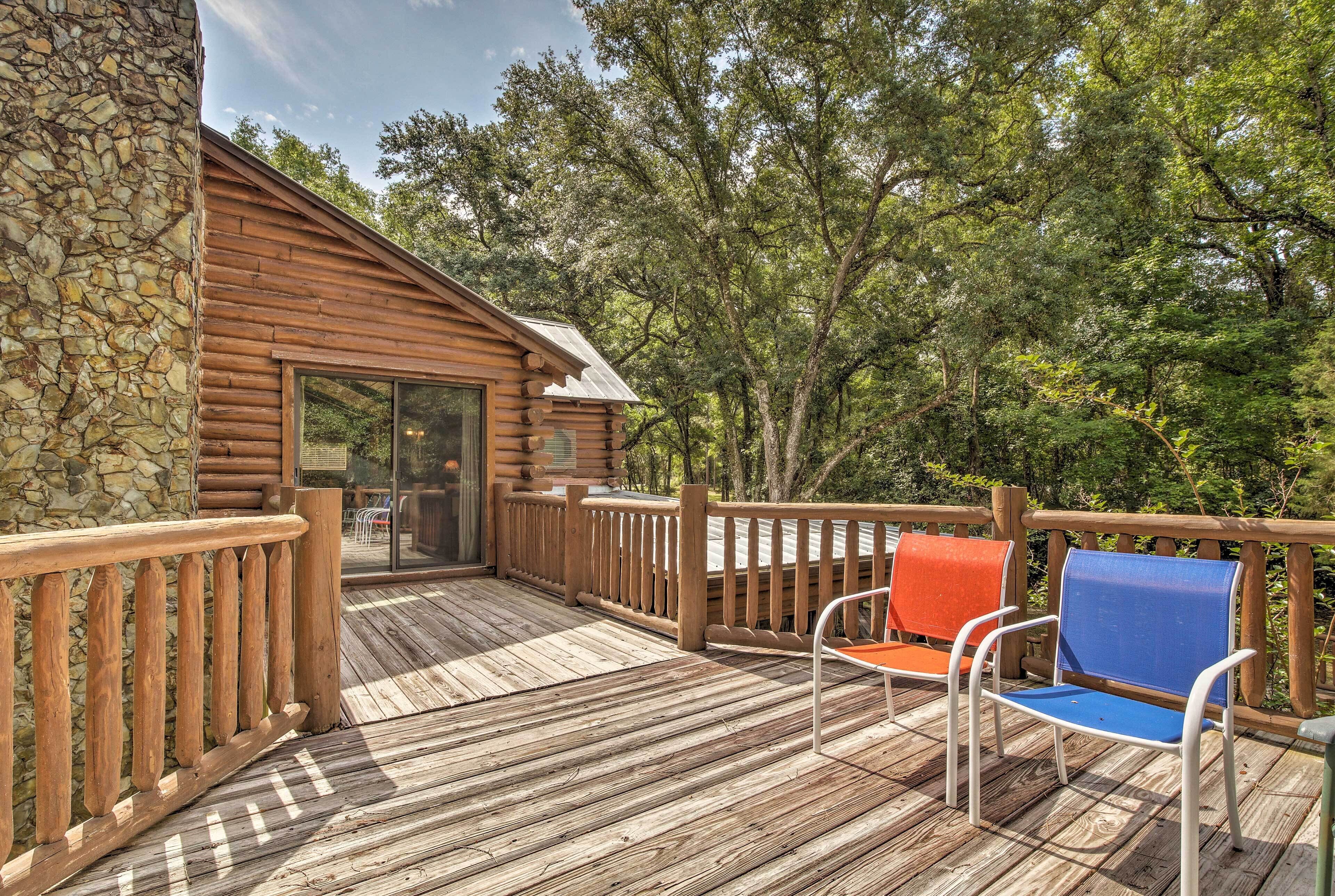 Een vakantiehuisje van hout met een houten terras, een stenen muur en een glazen deur die leidt naar een terras met twee stoelen.