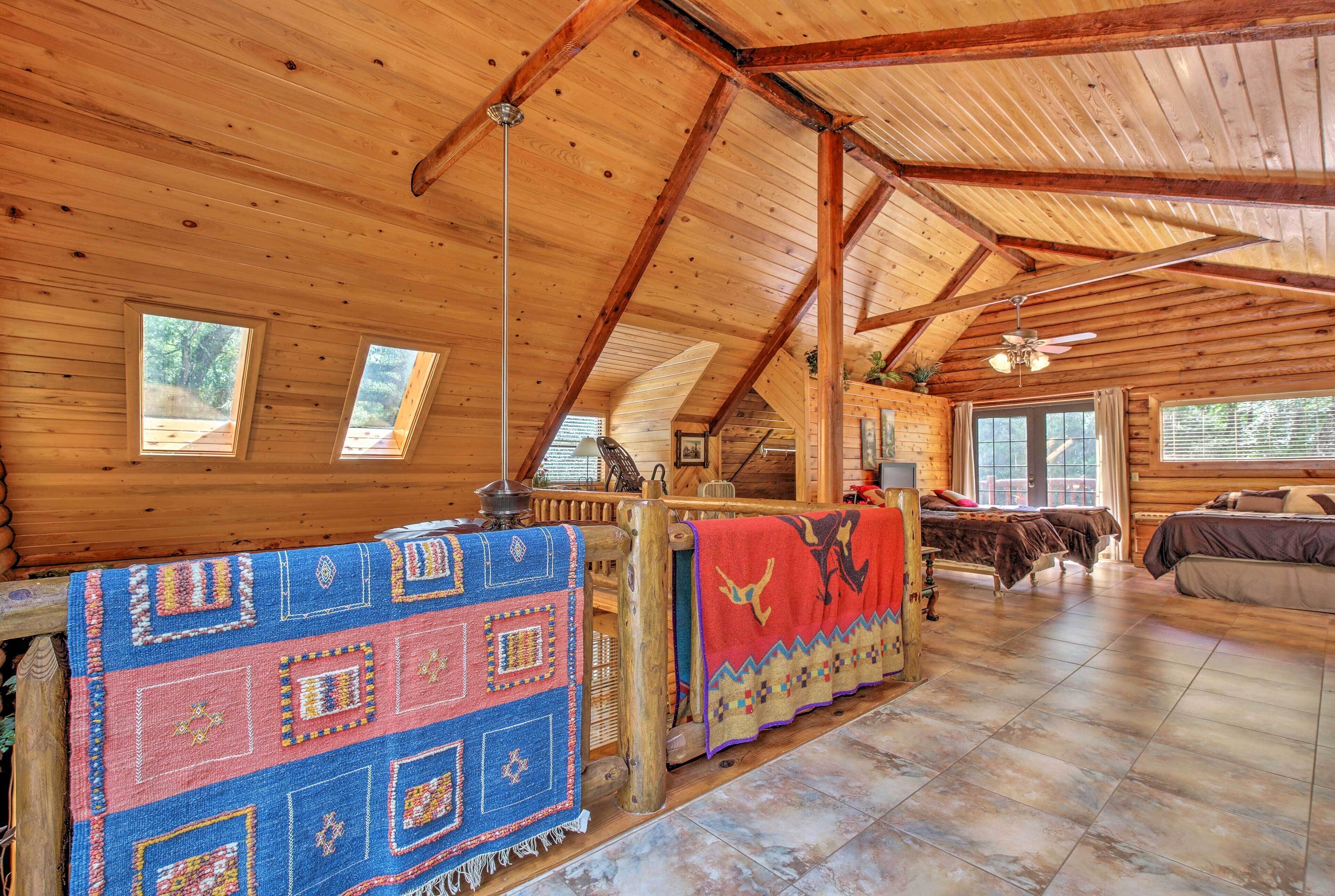 A spacious log cabin with high ceilings, a large bed, a fireplace, and a view of the outdoors through the windows.